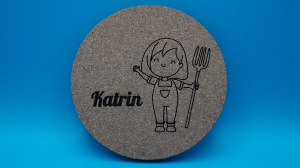 Personalisierbarer Untersetzer aus Kork mit niedlicher Gravur eines lächelnden Mädchens in Latzhose und Heugabel sowie einem individuell wählbaren Namen, hier „Katrin“. Perfekt als originelle Tischdeko, kreatives Geschenk oder persönliche Erinnerung an besondere Anlässe.