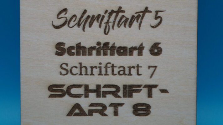 Nahaufnahme der unteren vier Gravuren auf Holz mit den Schriftarten 5 bis 8. Zu sehen sind: eine dynamische Schreibschrift, eine blockige Retro-Schrift, eine klassische Serifenschrift und eine moderne Techno-Schriftart.