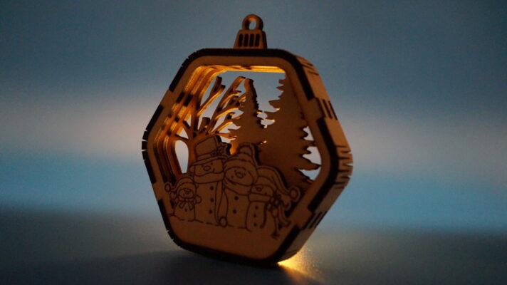 Mehrlagiges Weihnachtsornament mit einer Schneemannfamilie, Winterlandschaft und gelaserten Details. Von hinten beleuchtet zu einem schönen Schattenspiel.