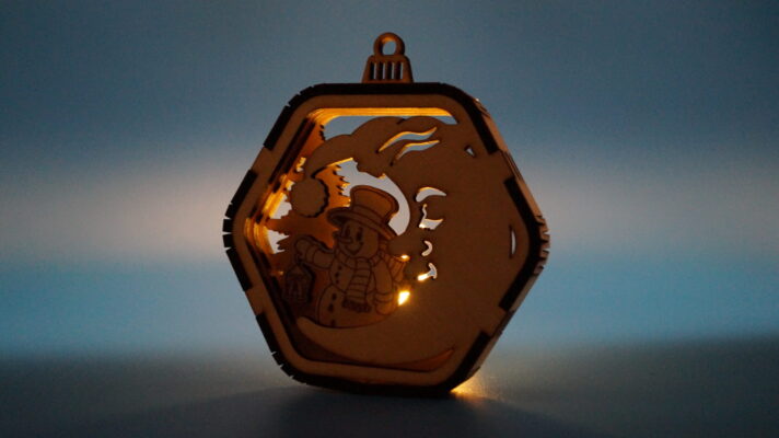 Weihnachtsornament aus Holz mit Mondmotiv, Schneemann und mehrschichtigem Design. Von hinten durch ein Teelicht beleuchtet